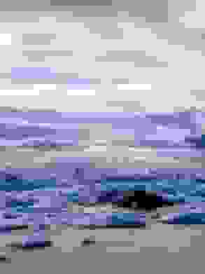 Under mixed clouds, a glacier rolls down a hillside, with a glacier lagoon in the foreground