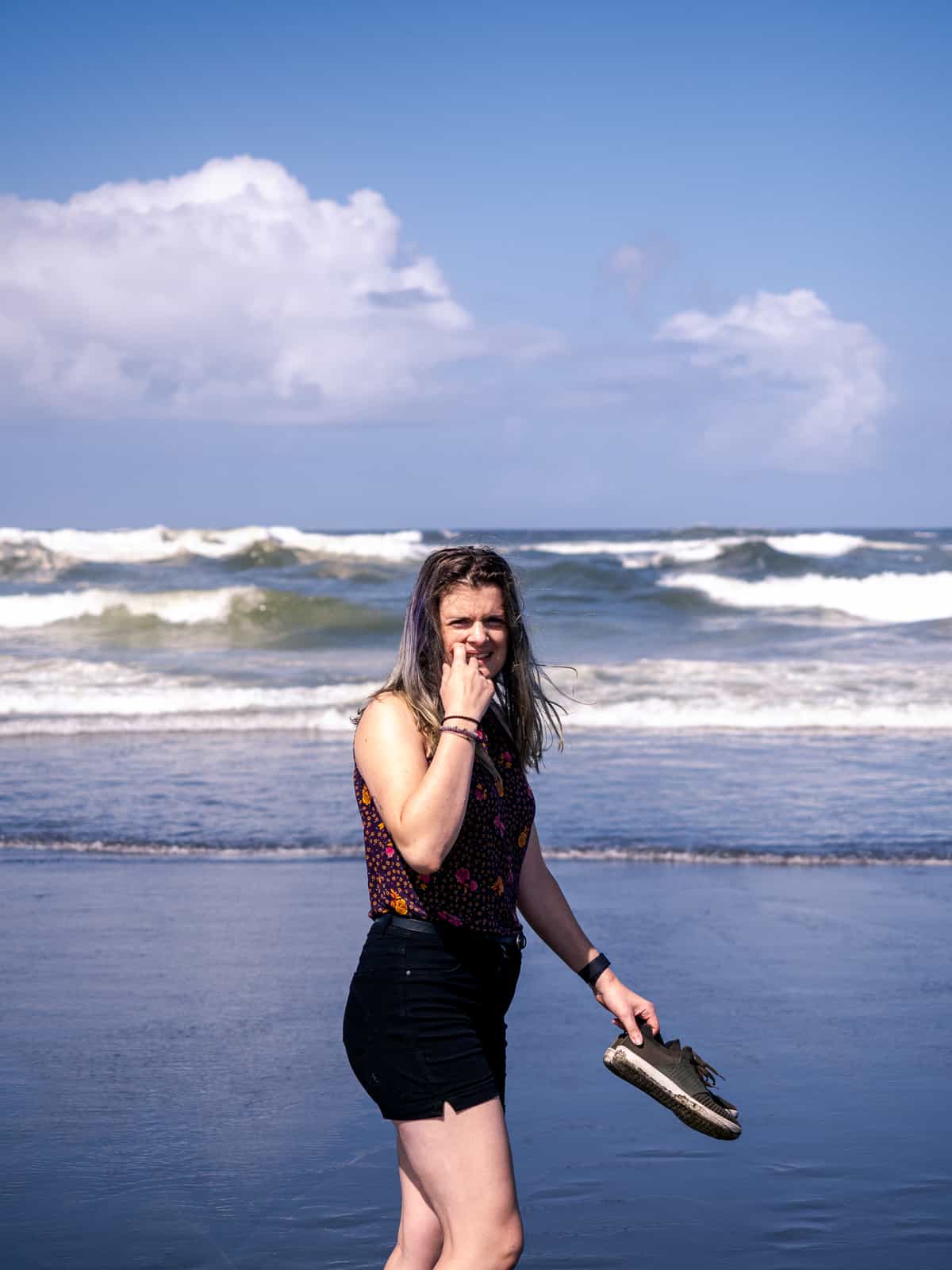 A woman walking along an ocean beach holding her shoes