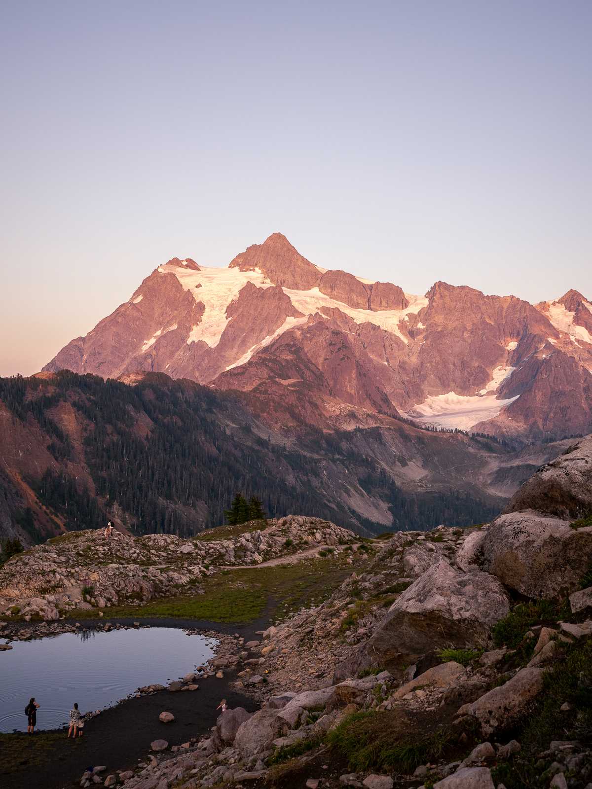 Mountain ridges lit with sunset glow, people in the foreground.