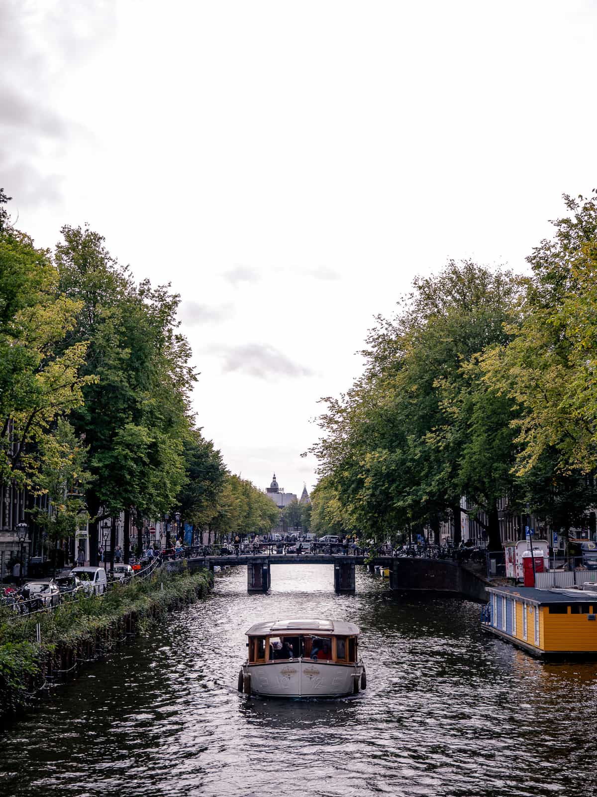 A daytime view down a canal in Amsterdam, with a river boat floating down the center