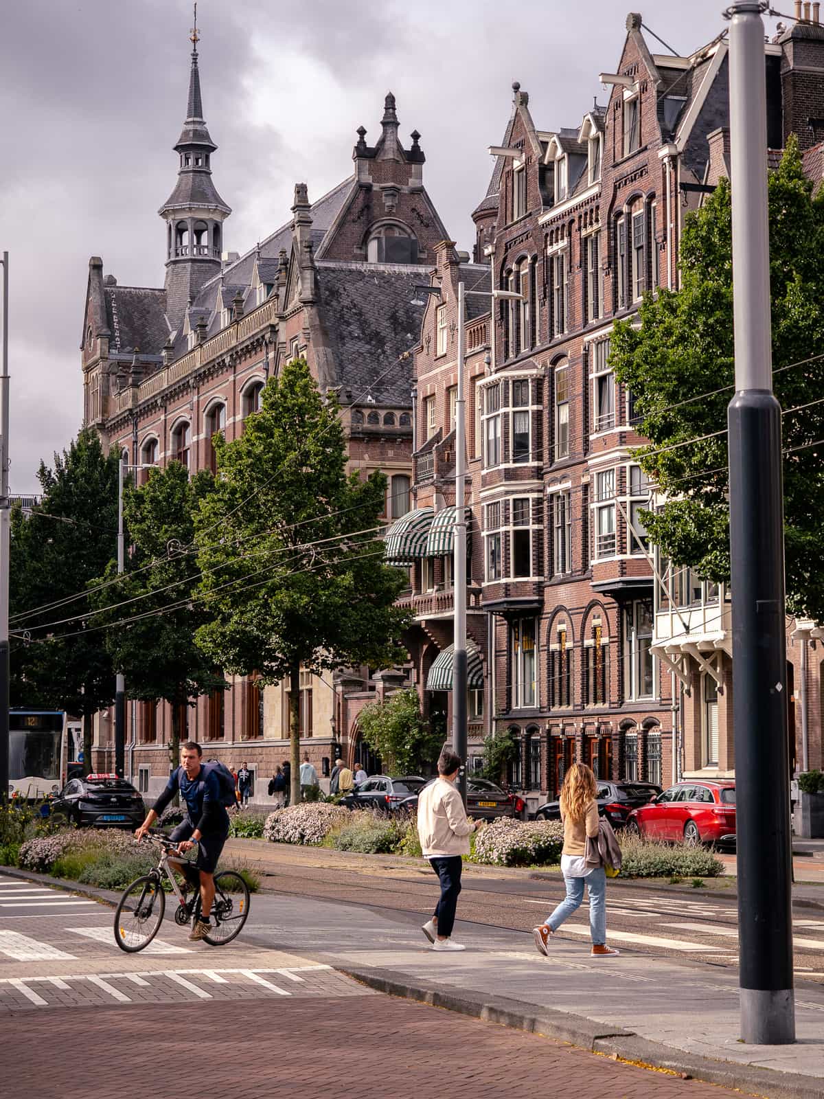 A bicyclist and pedestrians walk in from of historic architecture in Amsterdam