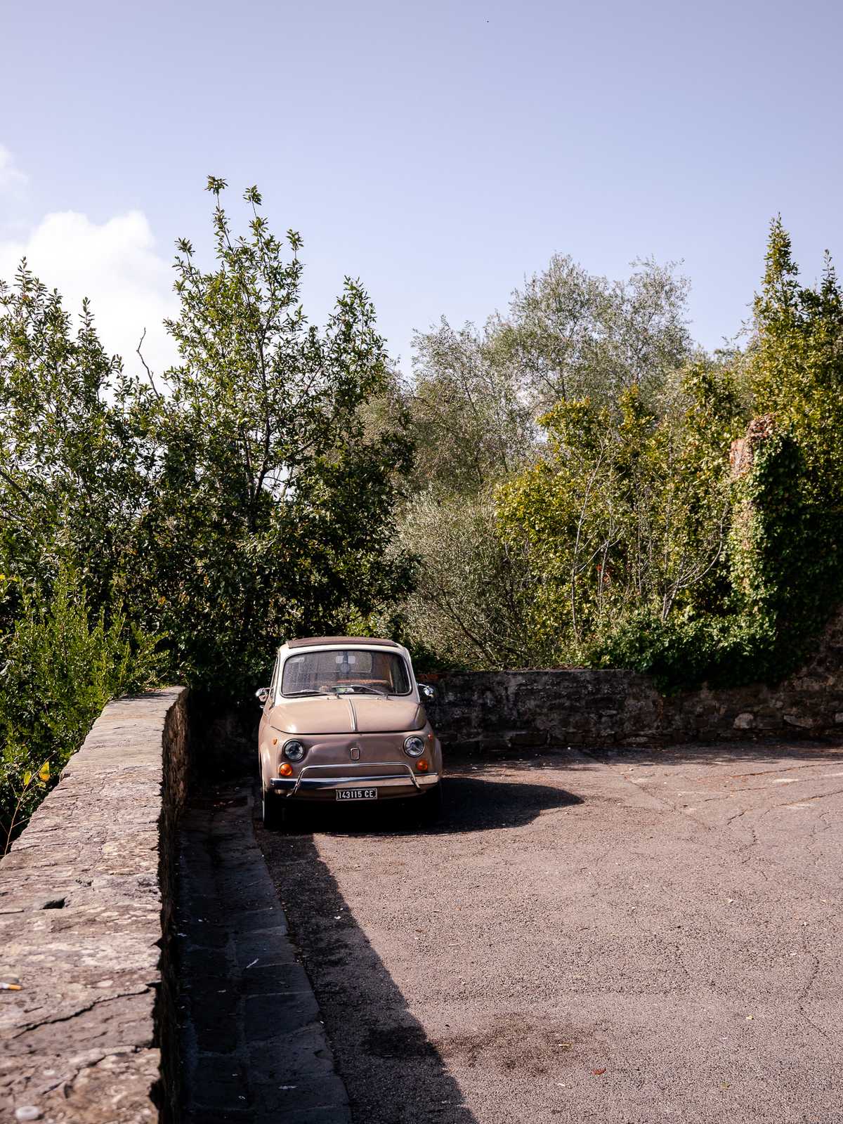 A small, old European car parked along a stone fence