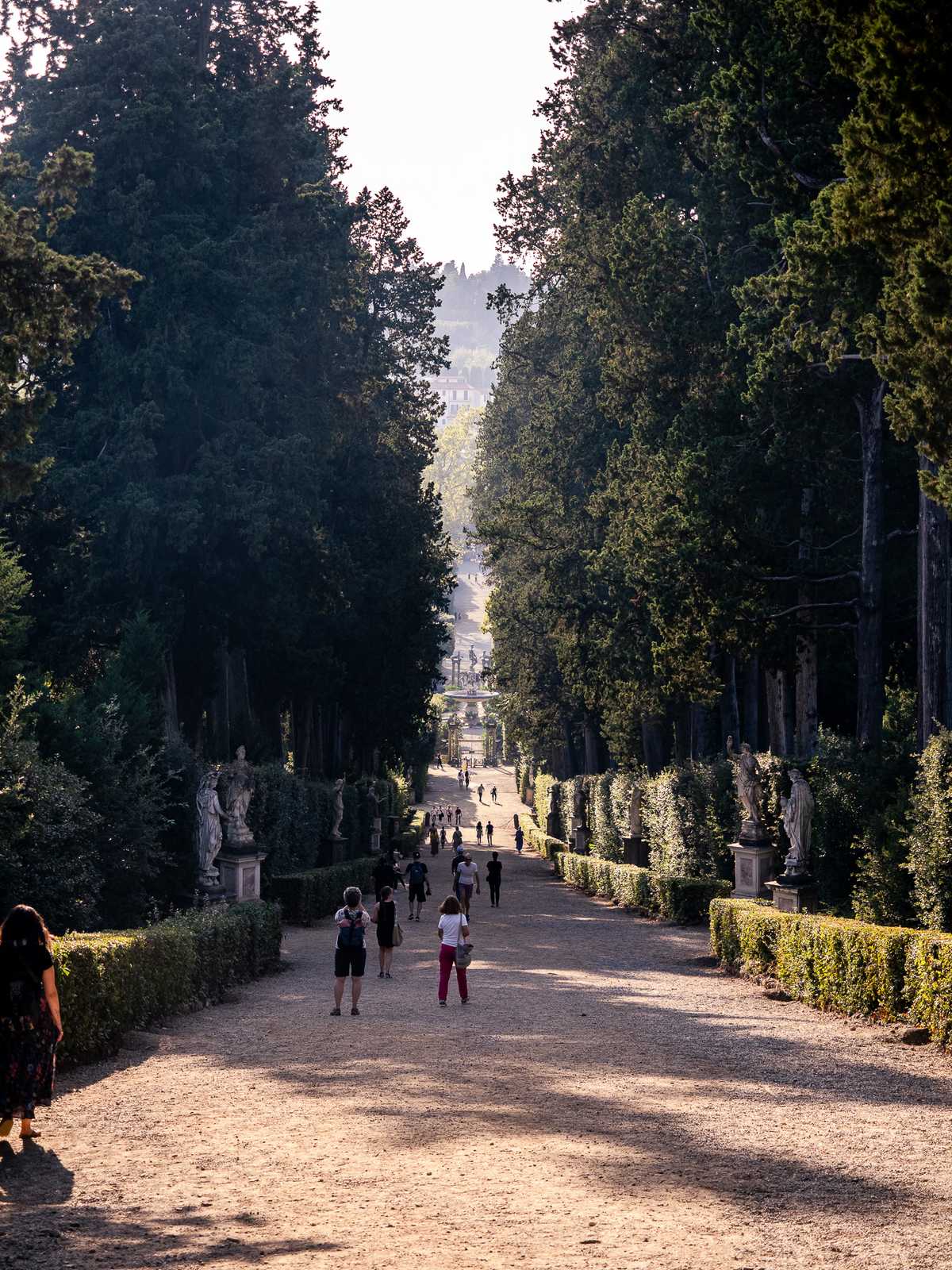 Extending far into the distance, a wide gravel promenade, lined with green hedges and trees