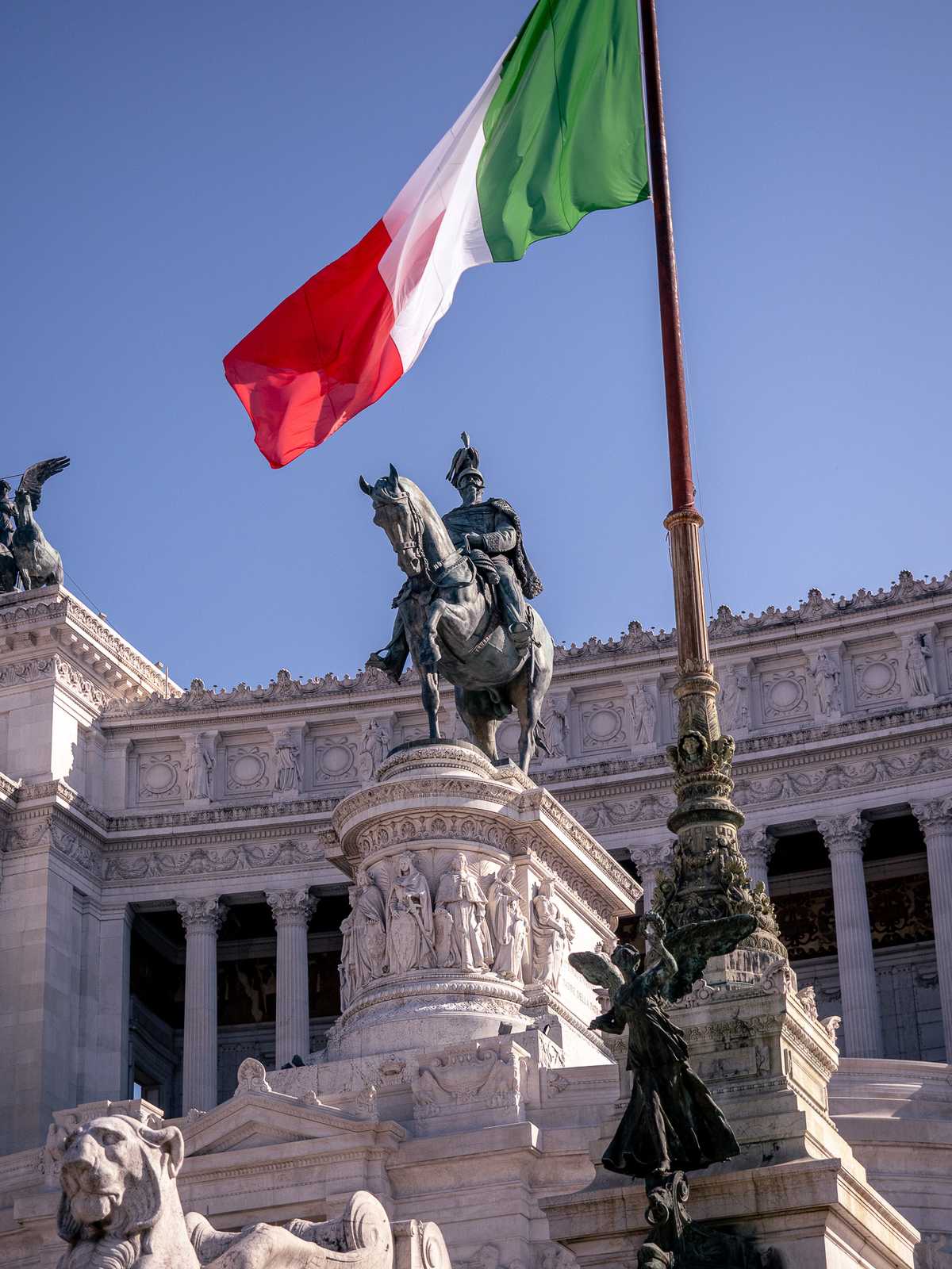 The Italian flag waves above a government building and bronze statue 