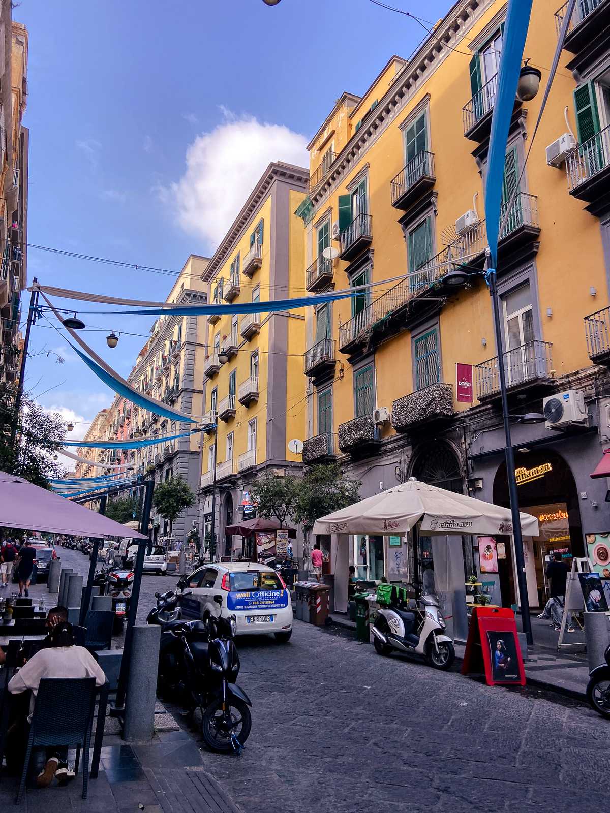 Banners span across a road between yellow-painted buildings in Naples