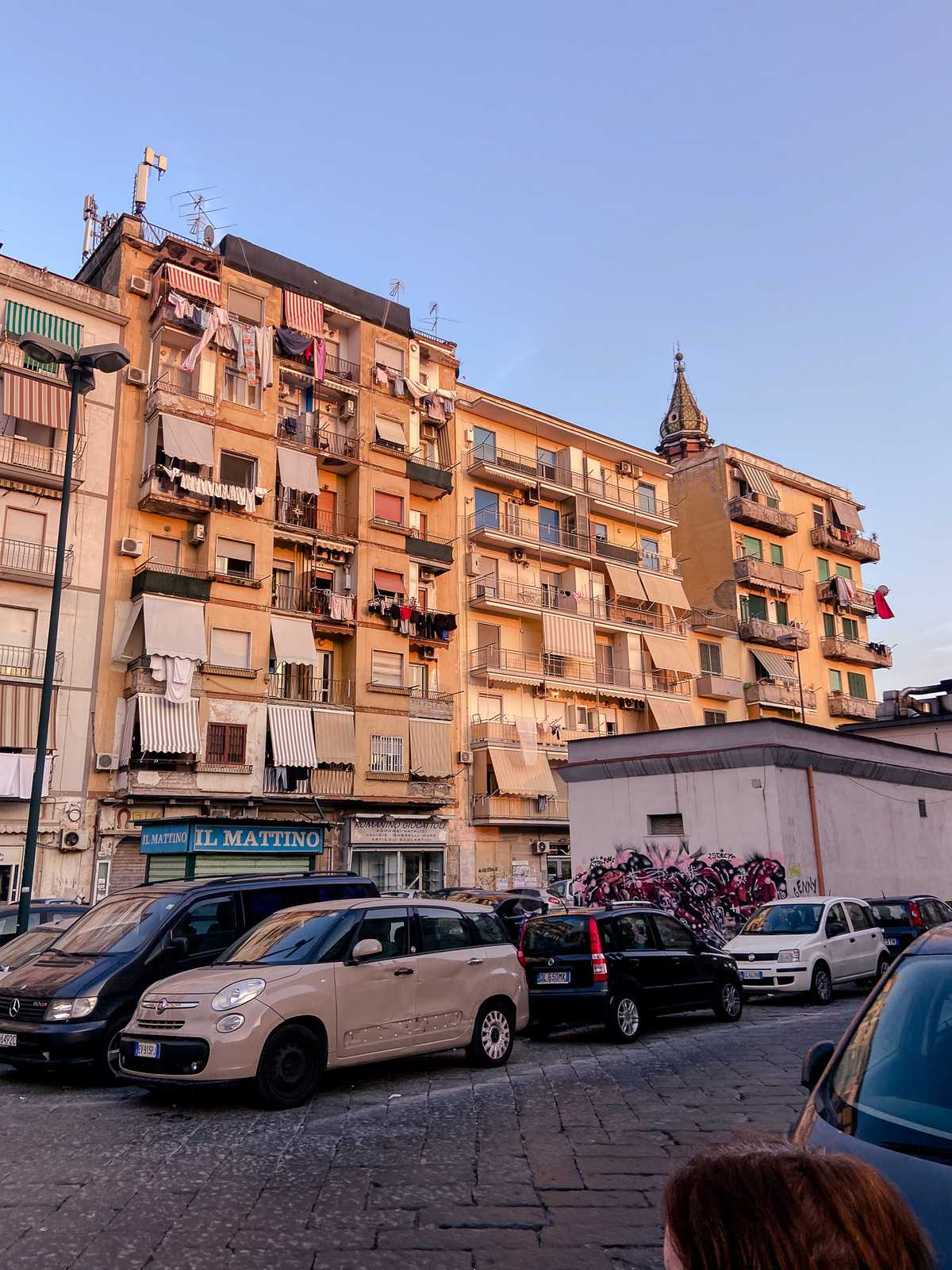 Sunset colors reflect off an apartment building with European cars parked in front