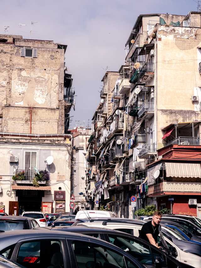 A man gets out of a car, with Naples apartments in the background, balconies covered in laundry and utilities