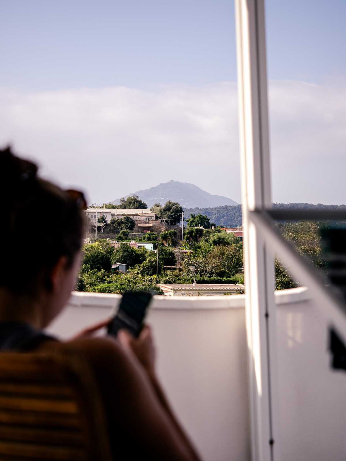 Someone looks at their phone, with trees and an island peak in the distance