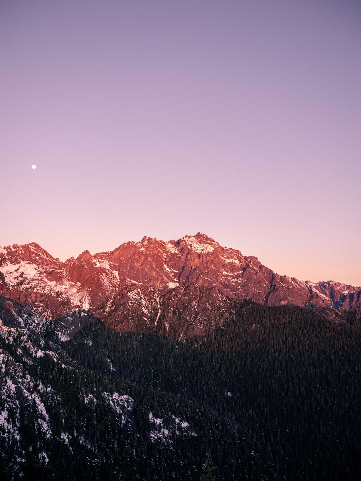 Mountain reflects the colors of sunrise with the moon visible in the sky