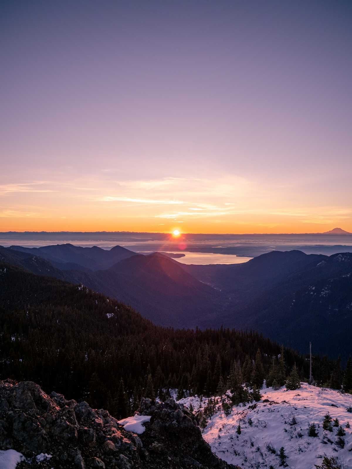 A wide ankle picture of a sunrise over the cascade mountains with Mount Rainier up to the far right