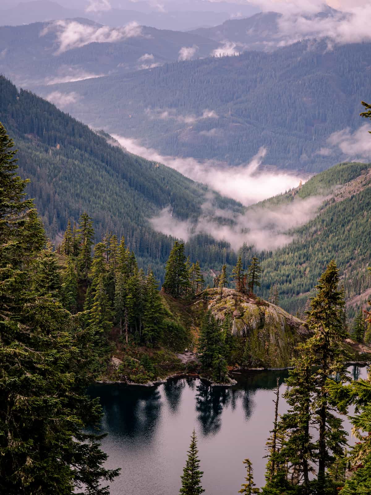 Clouds drift in a mountain valley with still-water in a pond in the foreground