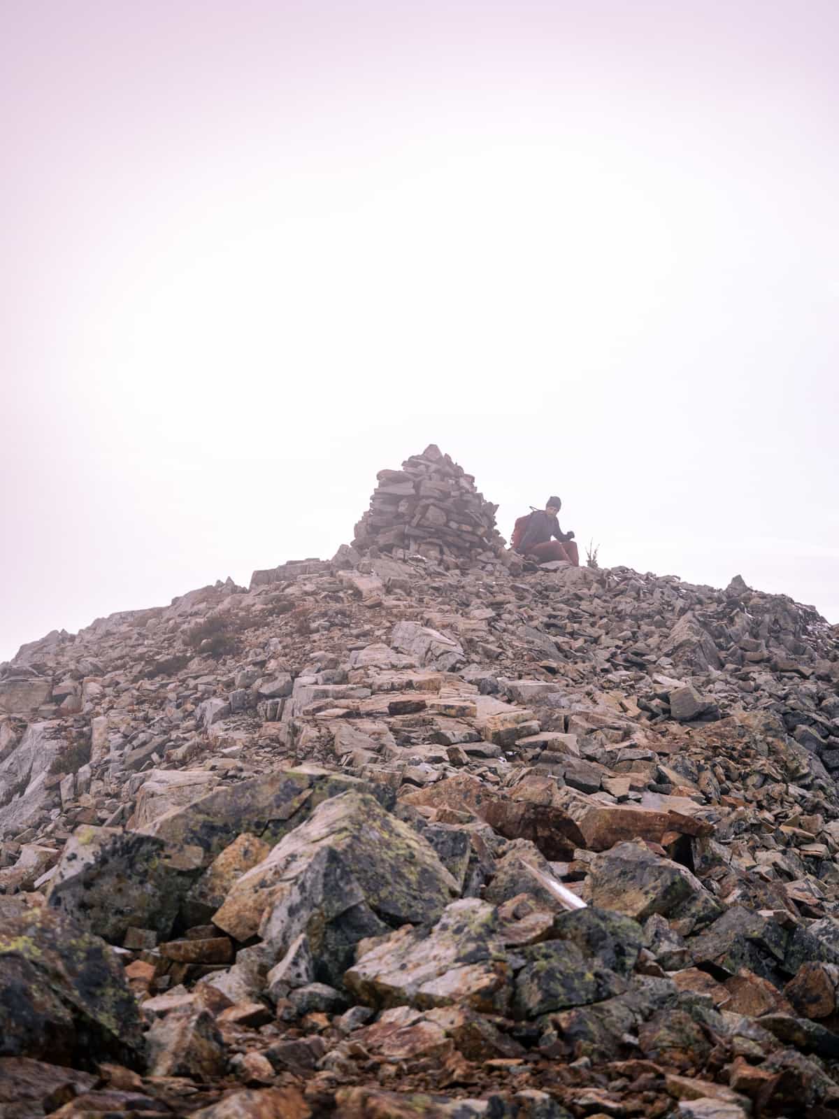 Person next to a column of stones at the top of a rocky mountain