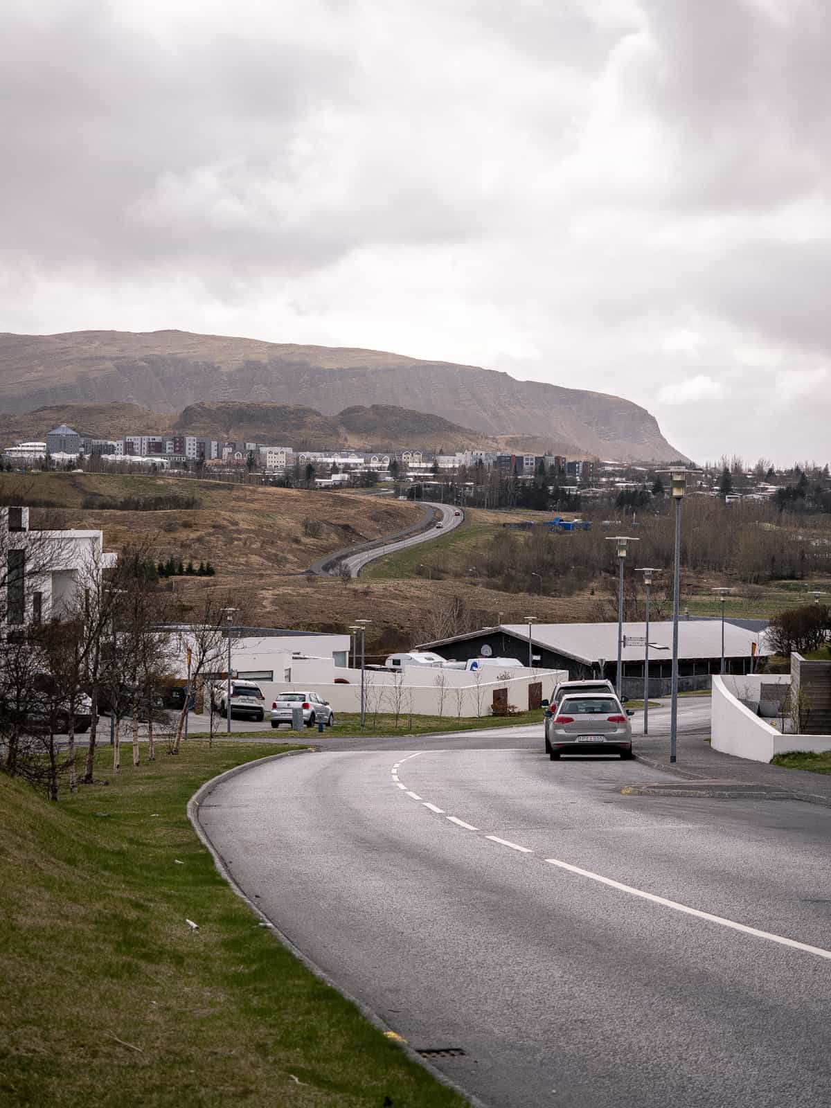 A road winds through rolling hills under a cloudy sky in Iceland.