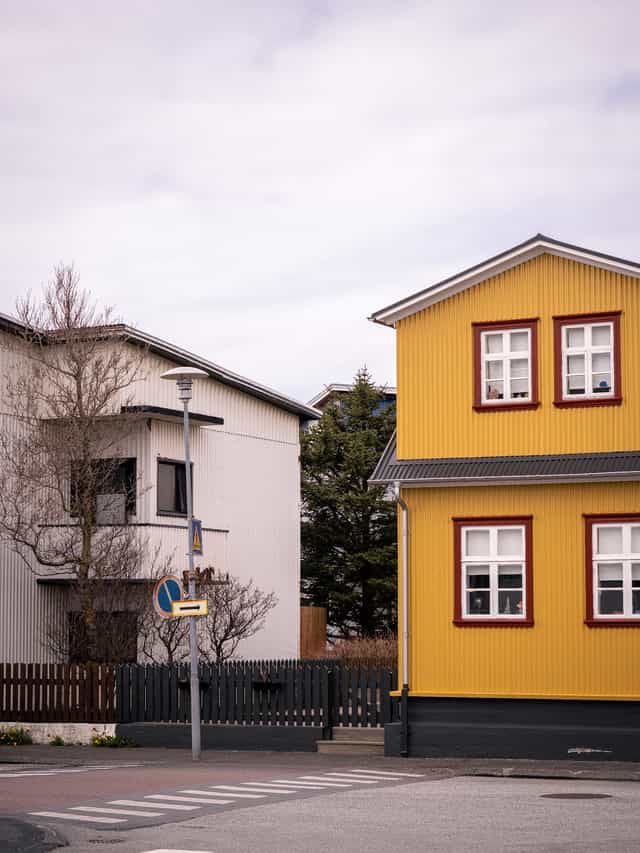 Neighborhood houses in an Icelandic town, white, and yellow with red trim.