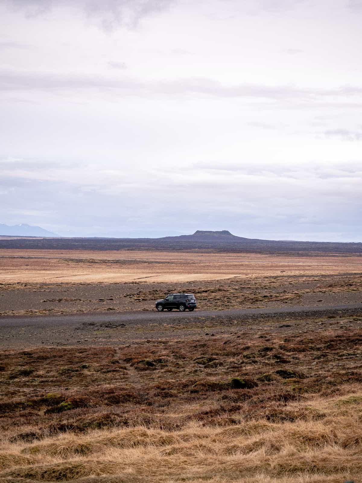 A small black car sits parked on a road cutting through brown and yellow plains.