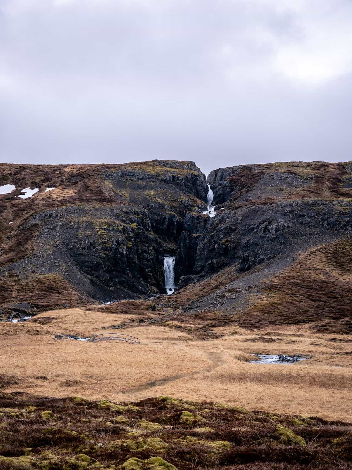 Two waterfalls fall down a ravine cut through a rolling hill