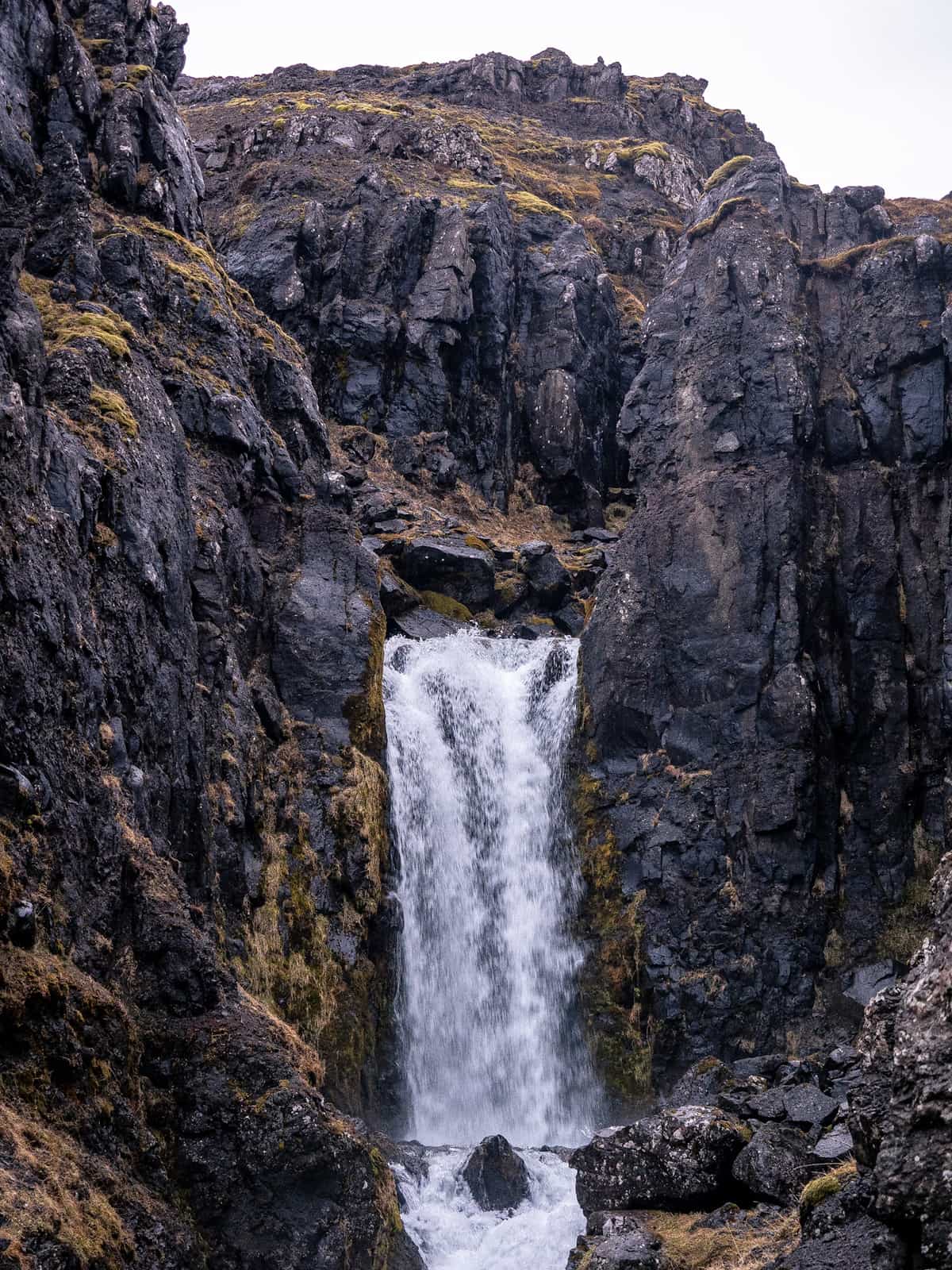 Water falls between two dark, moss-covered rock faces