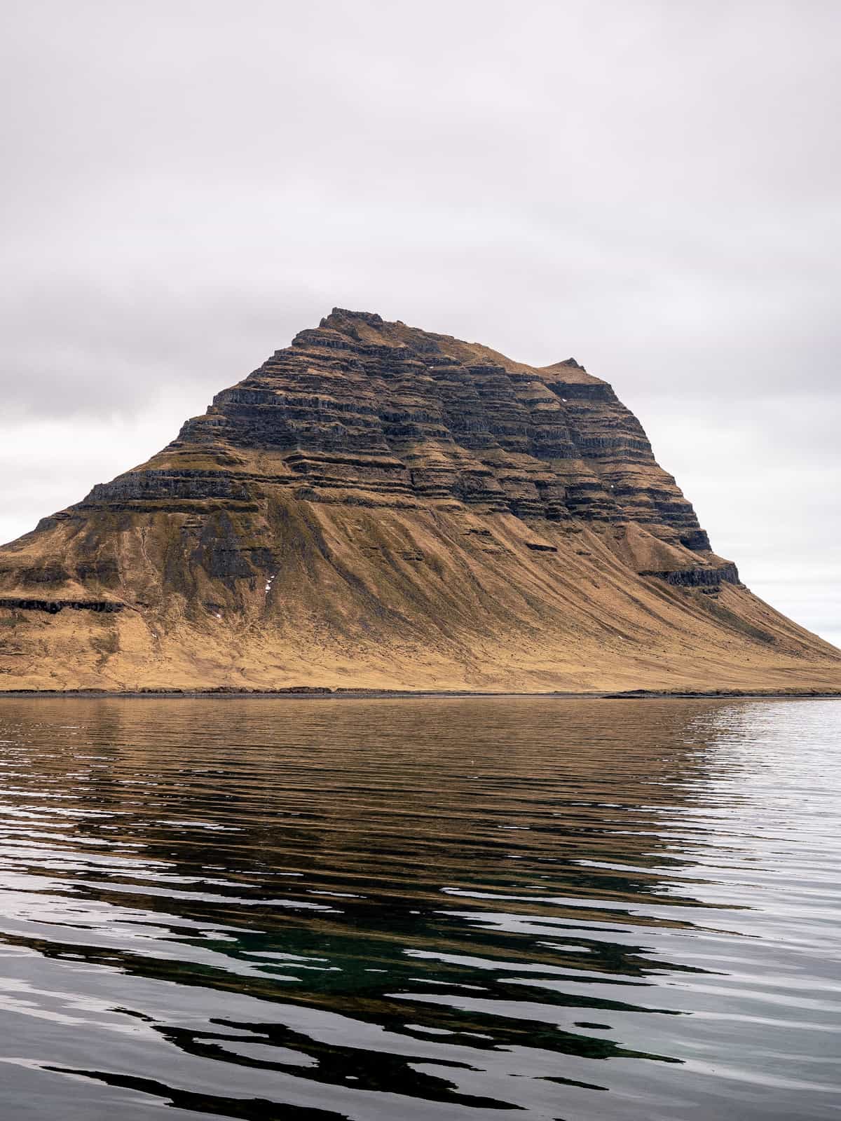 A singular tall mountain extends out of the ground, with wavey water in the foreground