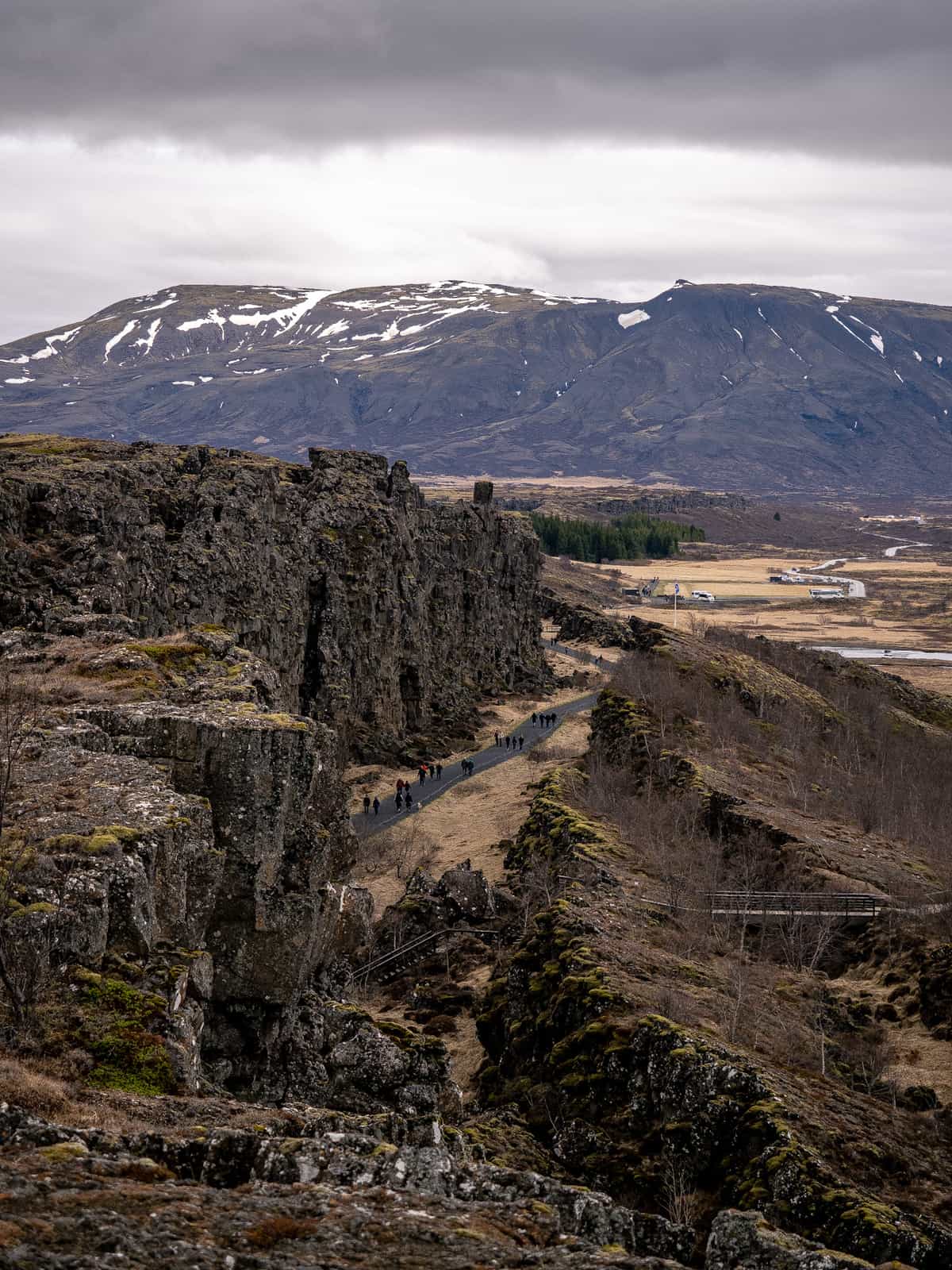 People walk down a pathway between two walls of rock, with mountains visible in the distance