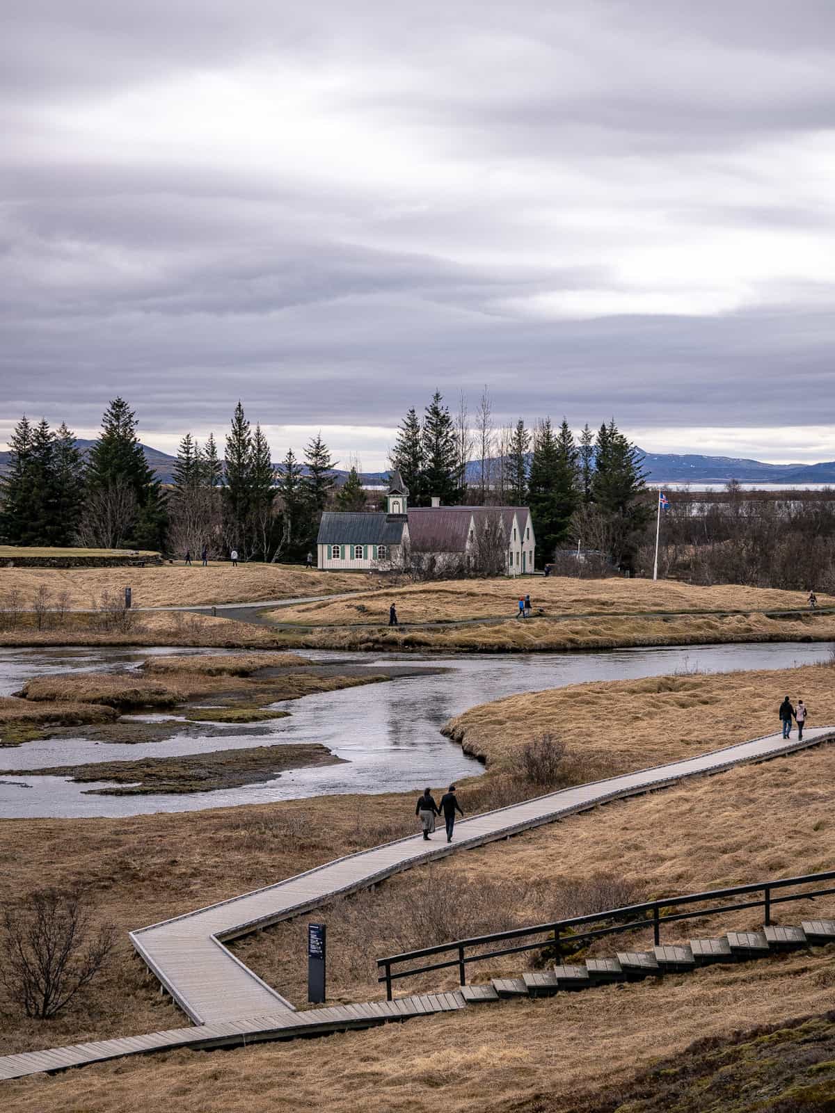 People walk on pathways next to a wandering river, with a church and building in the distance