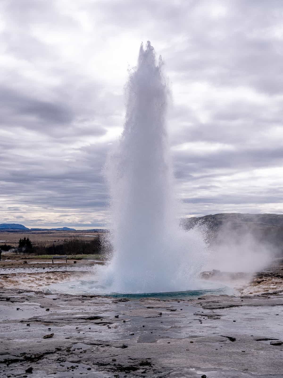 A geyser erupts under a cloudy sky