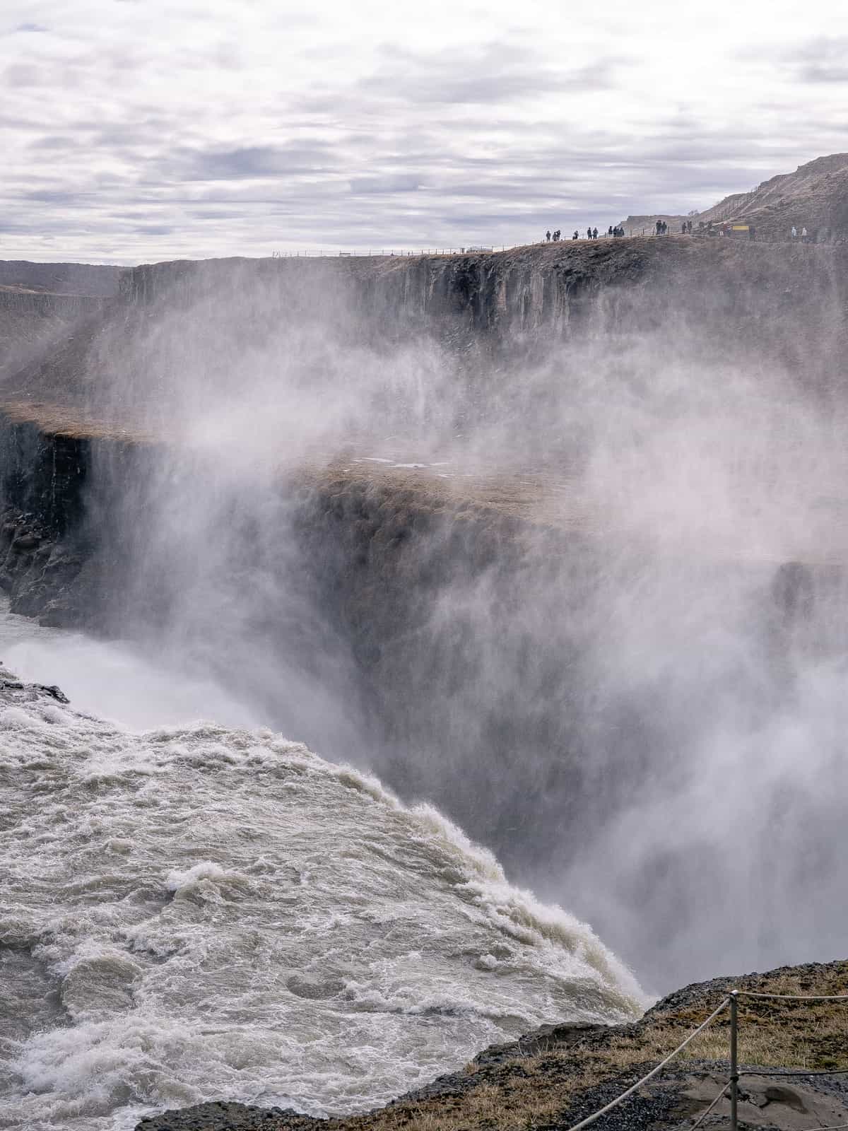 Water falls over the edge, with clouds of mist rising up from the ravine