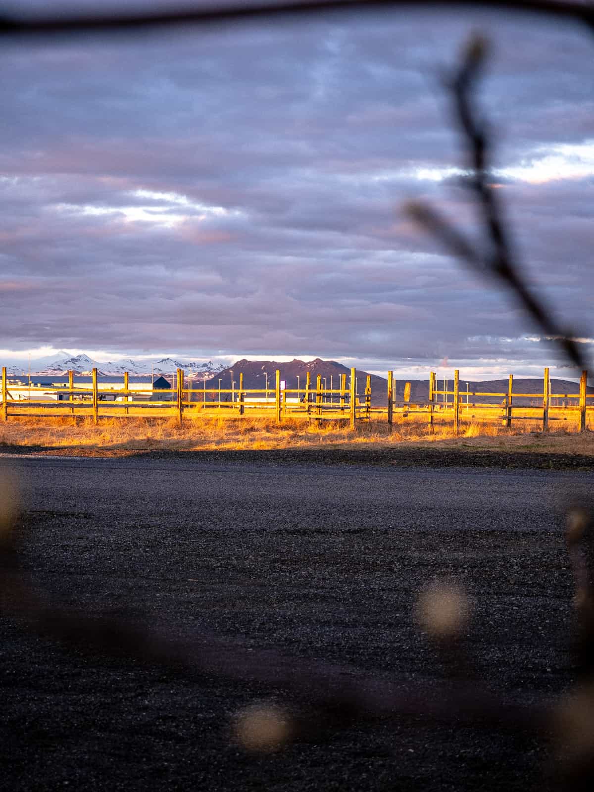 Golden sun reflects off of wooden fence, lighting up pink in clouds and catching mountains far away