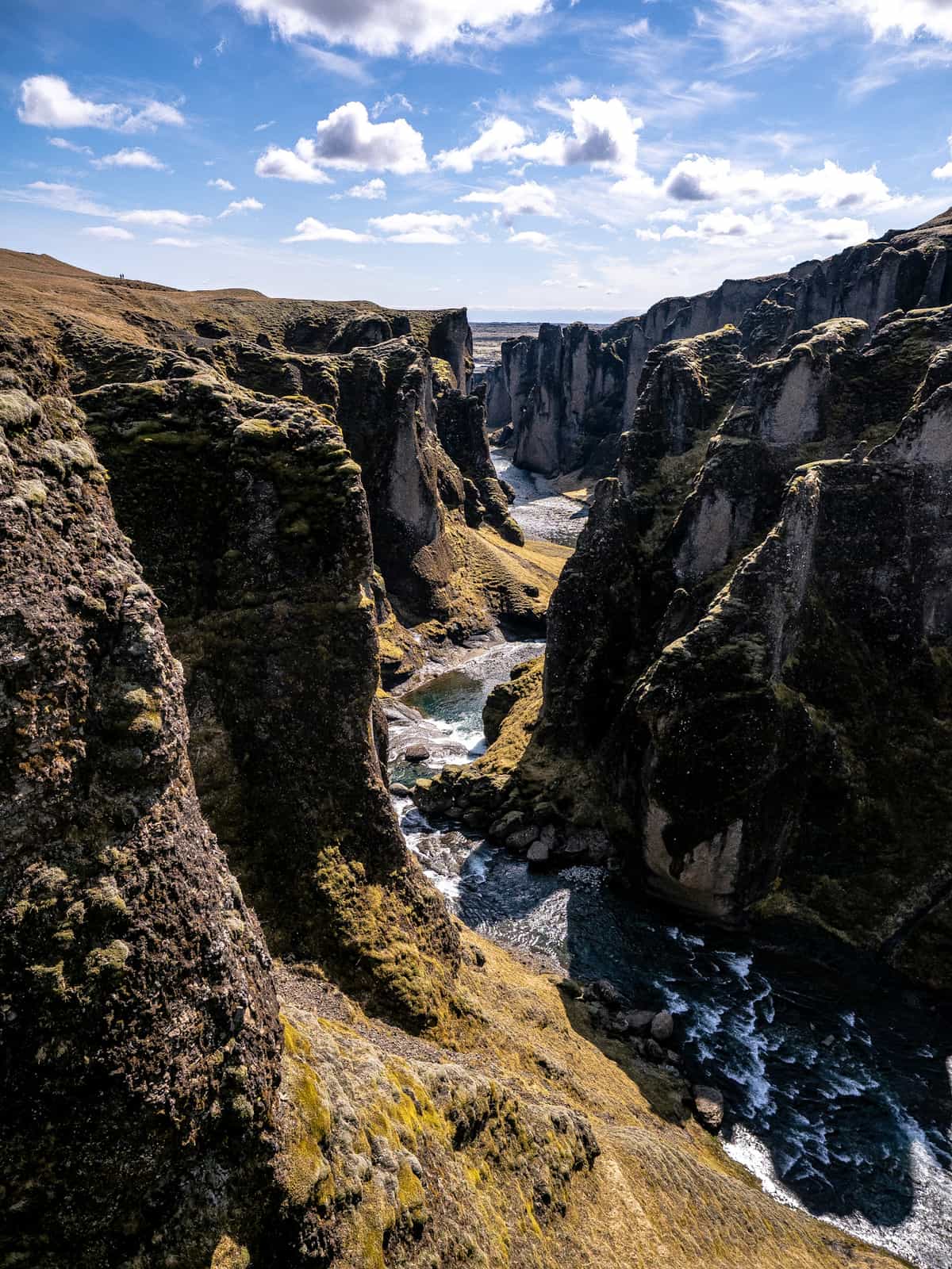 A serpent shaped canyon winds through a golden hillside, with plains in the distance