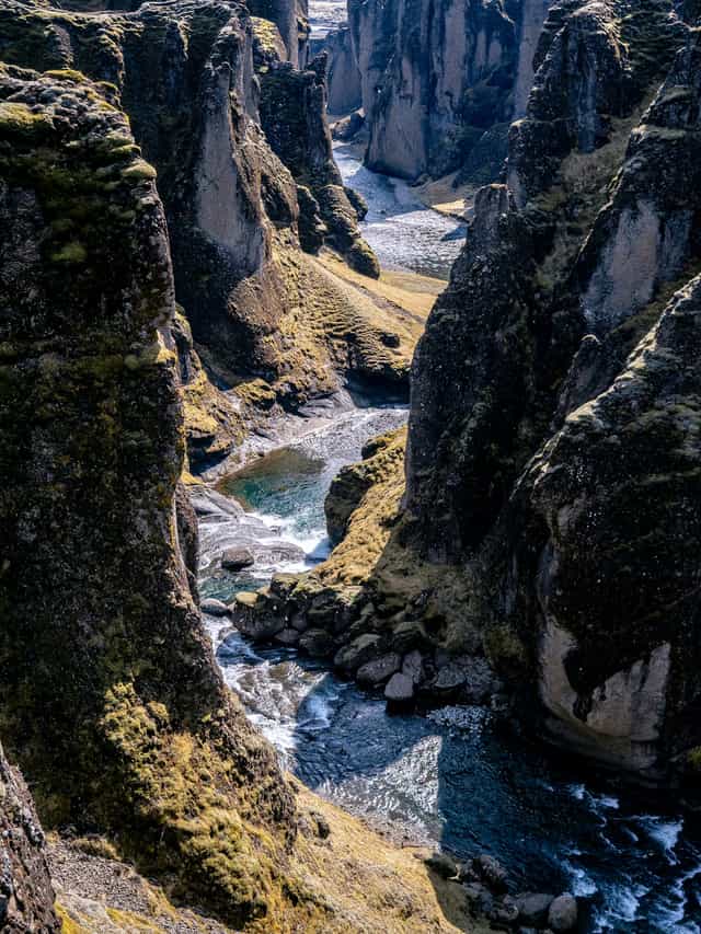 A serpent shaped canyon winds through a golden hillside, with blue rushing water at the bottom