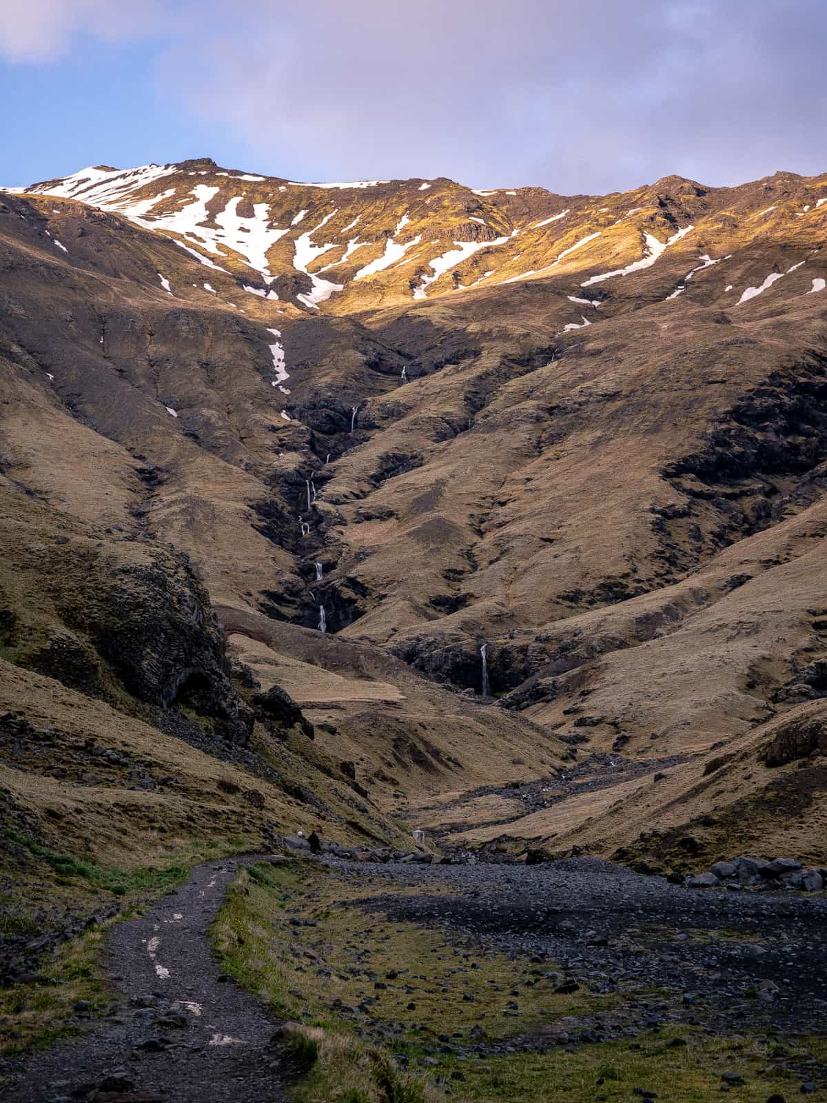 Sunset light shines on the top of a golden mountain with a chain of waterfalls cascading down