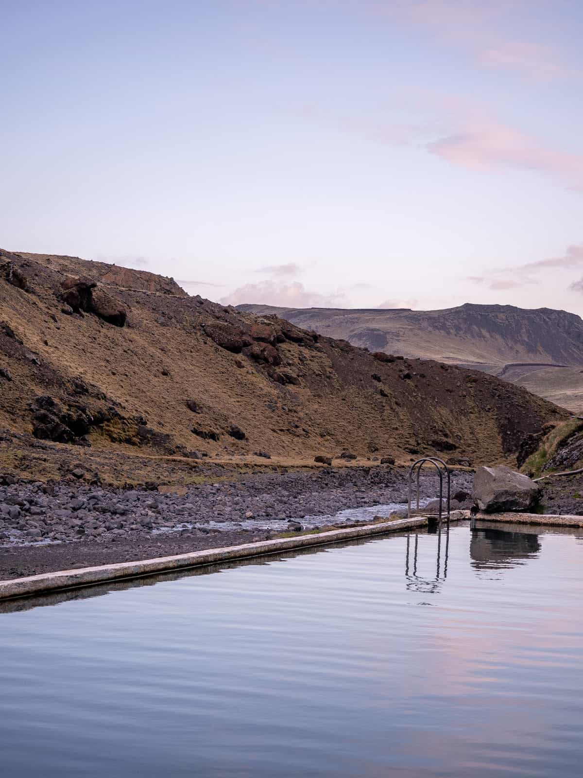 Pool water reflects the sunset colors, with rocky hillsides in the distance