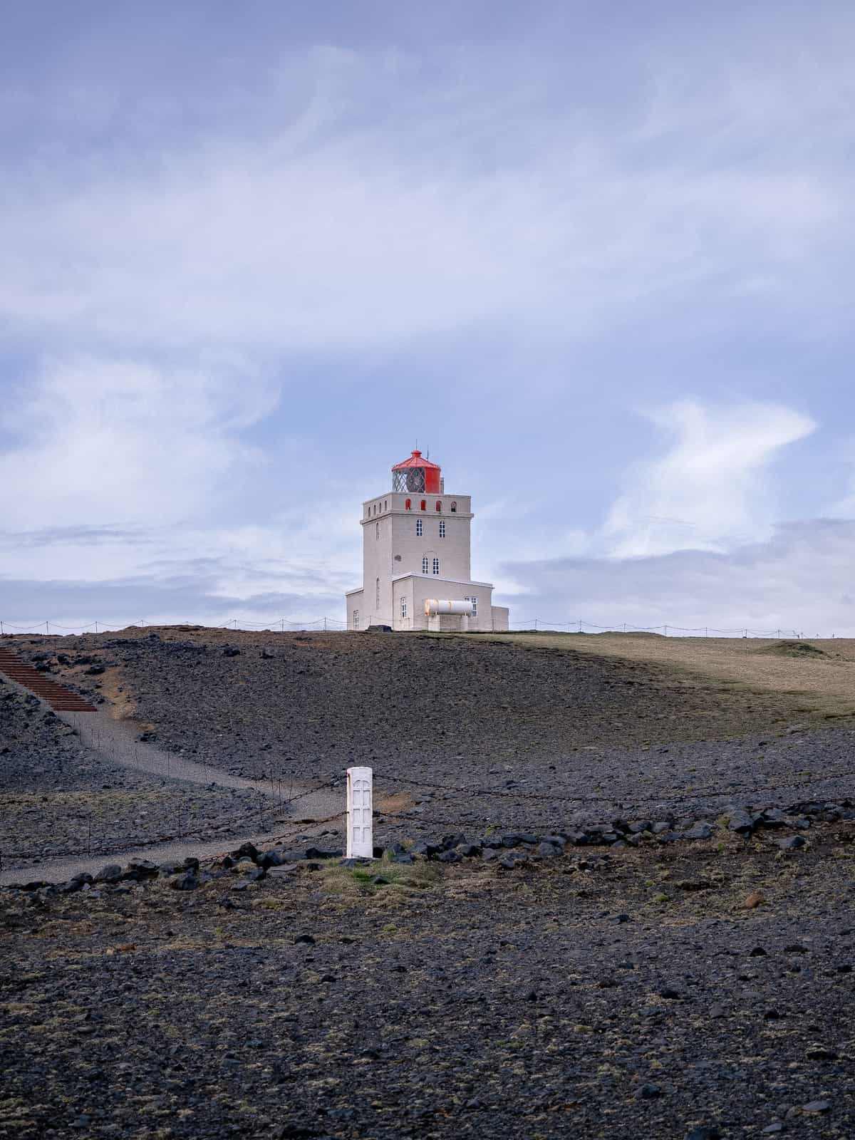 A white and orange lighthouse sits atop a black, rocky hillside