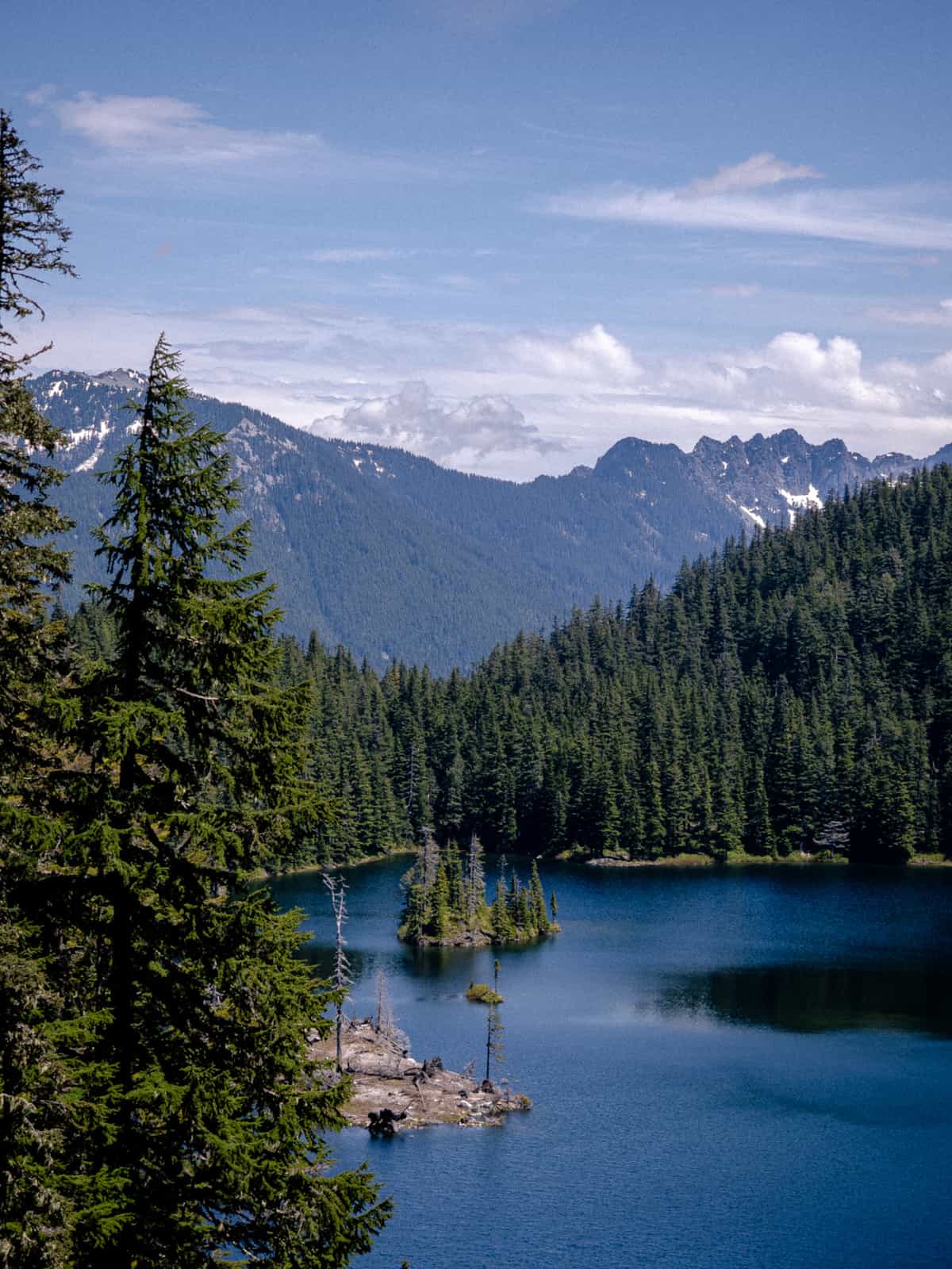 A zoomed in view of Thompson Lake with snowy mountain caps in the distance and a small island in the middle of the lake covered in pine trees