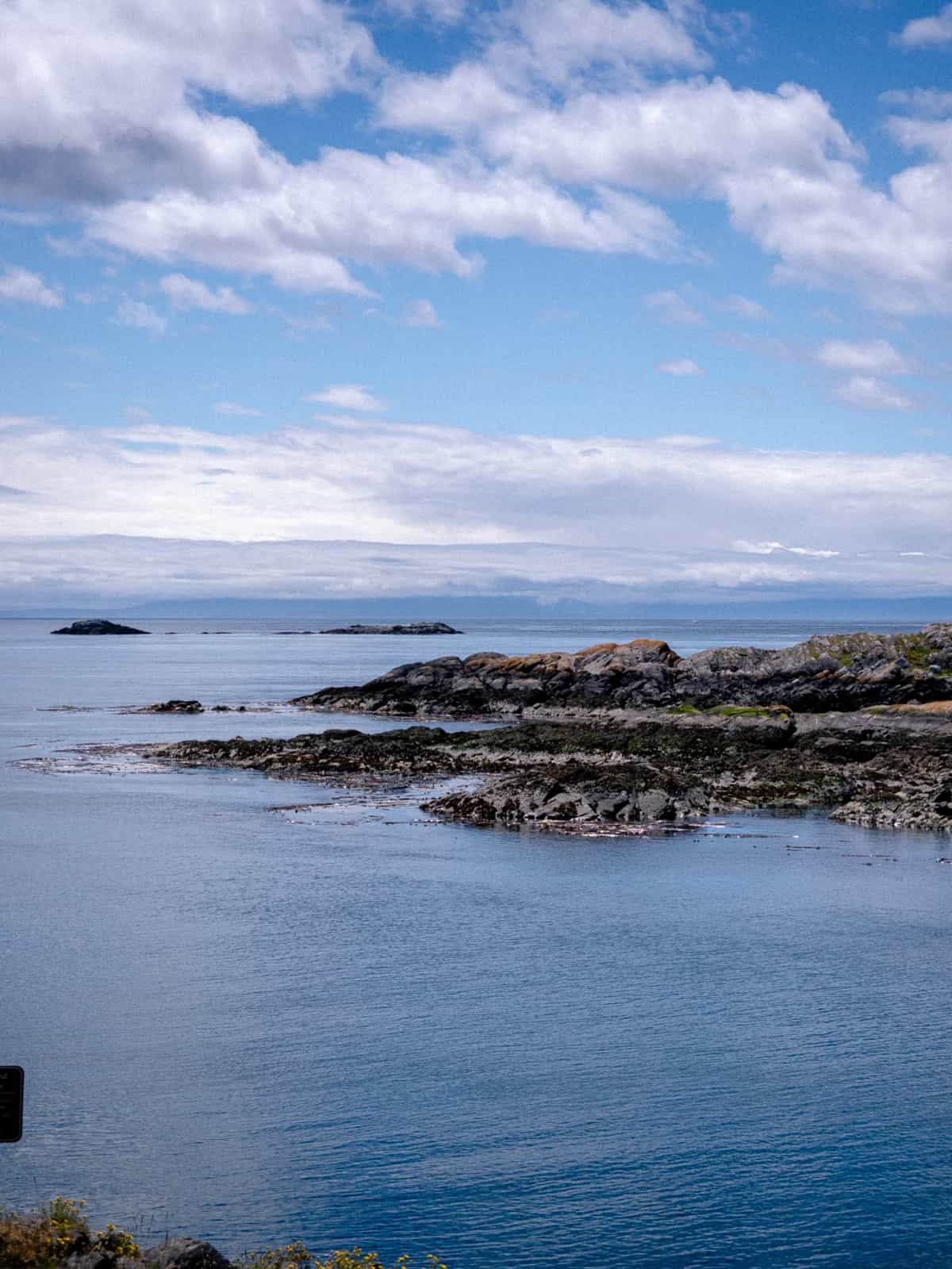 Rows of rocks rise out of the ocean with mountains, visible in the far distance